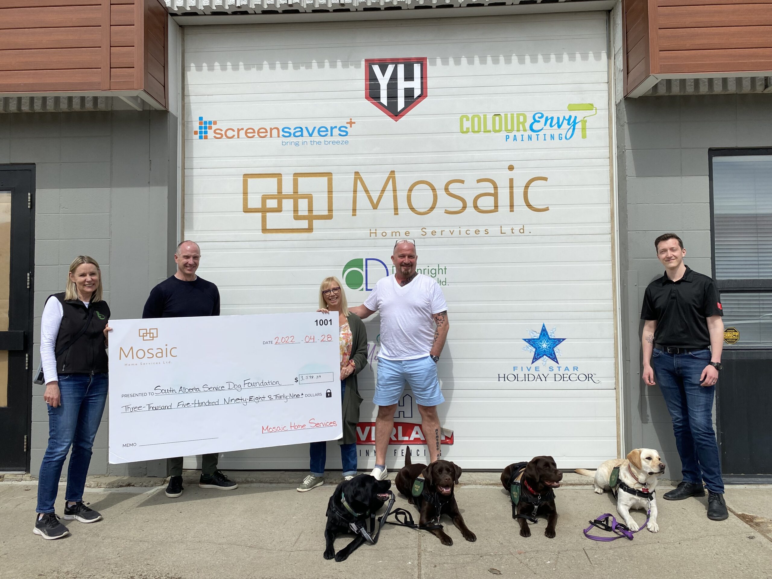 people giving a charity donation cheque in front of a building with dogs